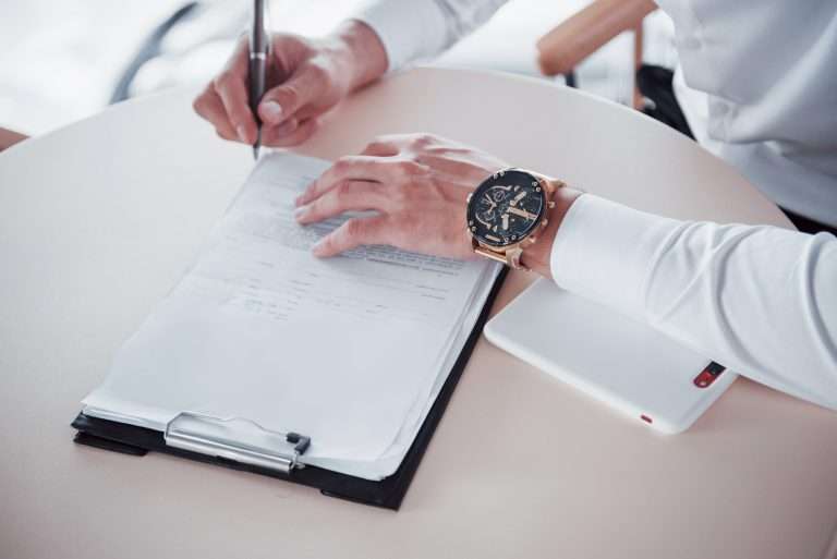 Person signing document, luxury watch visible.