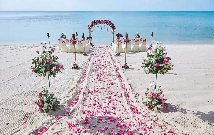 Beach wedding aisle with floral decorations and sea backdrop.