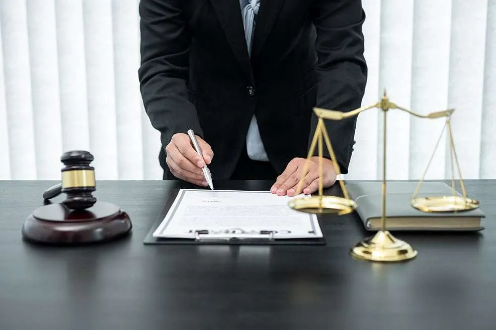 Lawyer signing document with gavel and scales of justice.