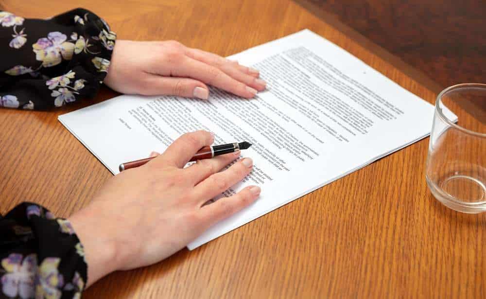 Person reviewing document before signing, on wooden table.