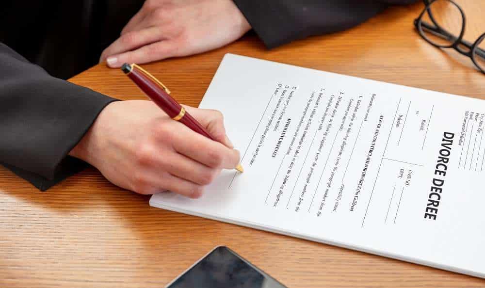 Person signing divorce decree document on desk.