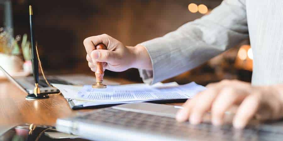 Person stamping document beside laptop.