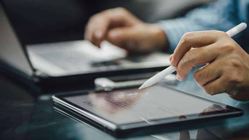 Person using stylus on digital tablet near laptop.