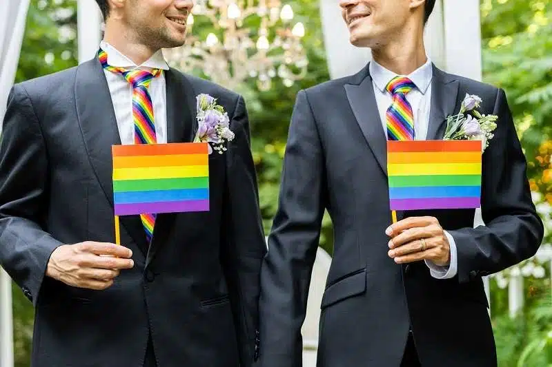 Same-sex wedding with rainbow ties and flag.