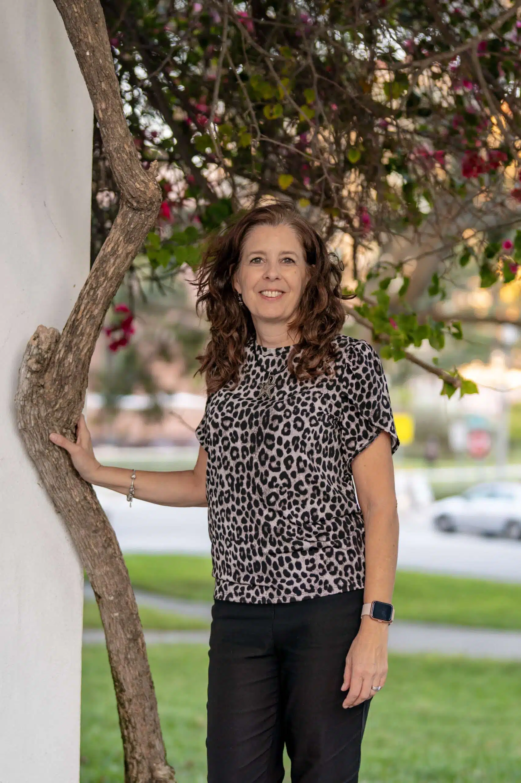 Woman smiling in leopard print top by tree.